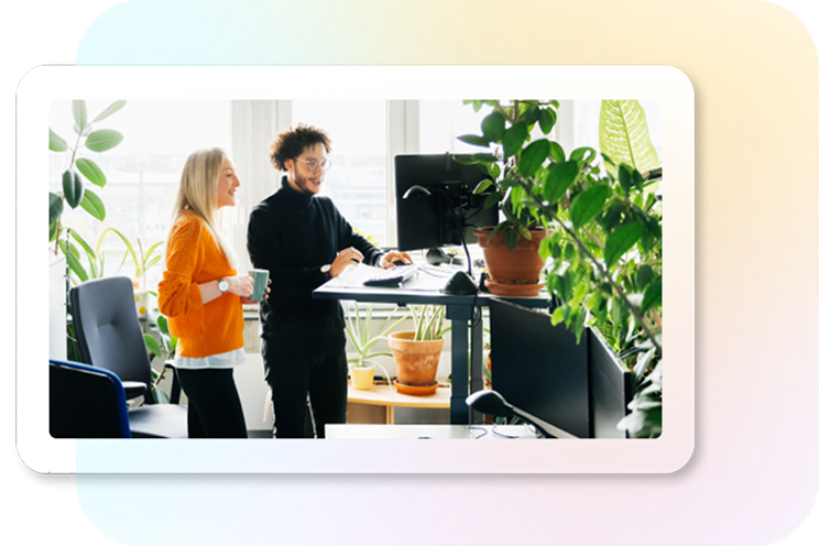Two people view external monitor in office with plants