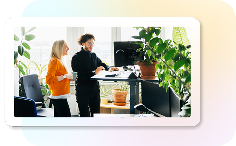 Two people view external monitor in office with plants